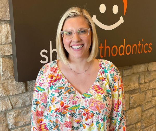 Woman smiling in front of Shine Orthodontics sign